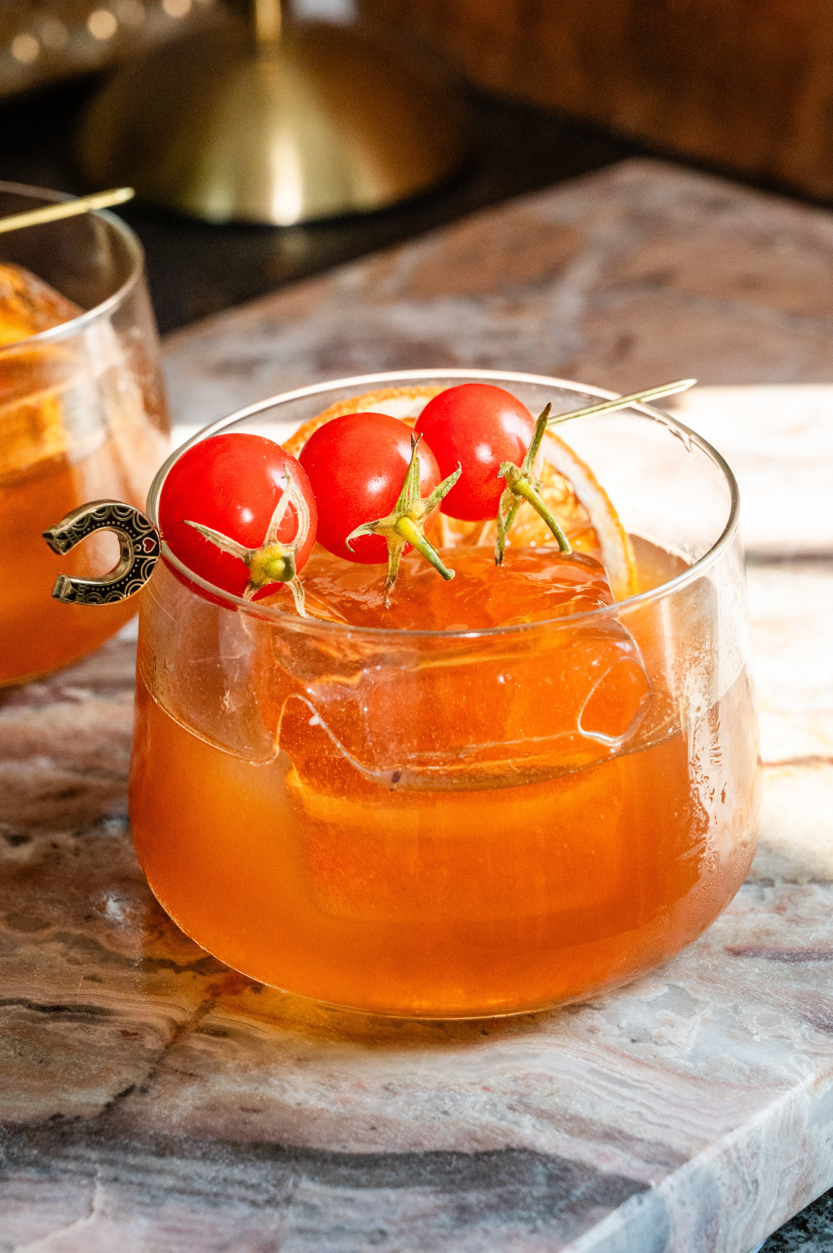 The truffle and tomato old fashioned on a pink marble slab and garnish with 3 cherry tomatoes .