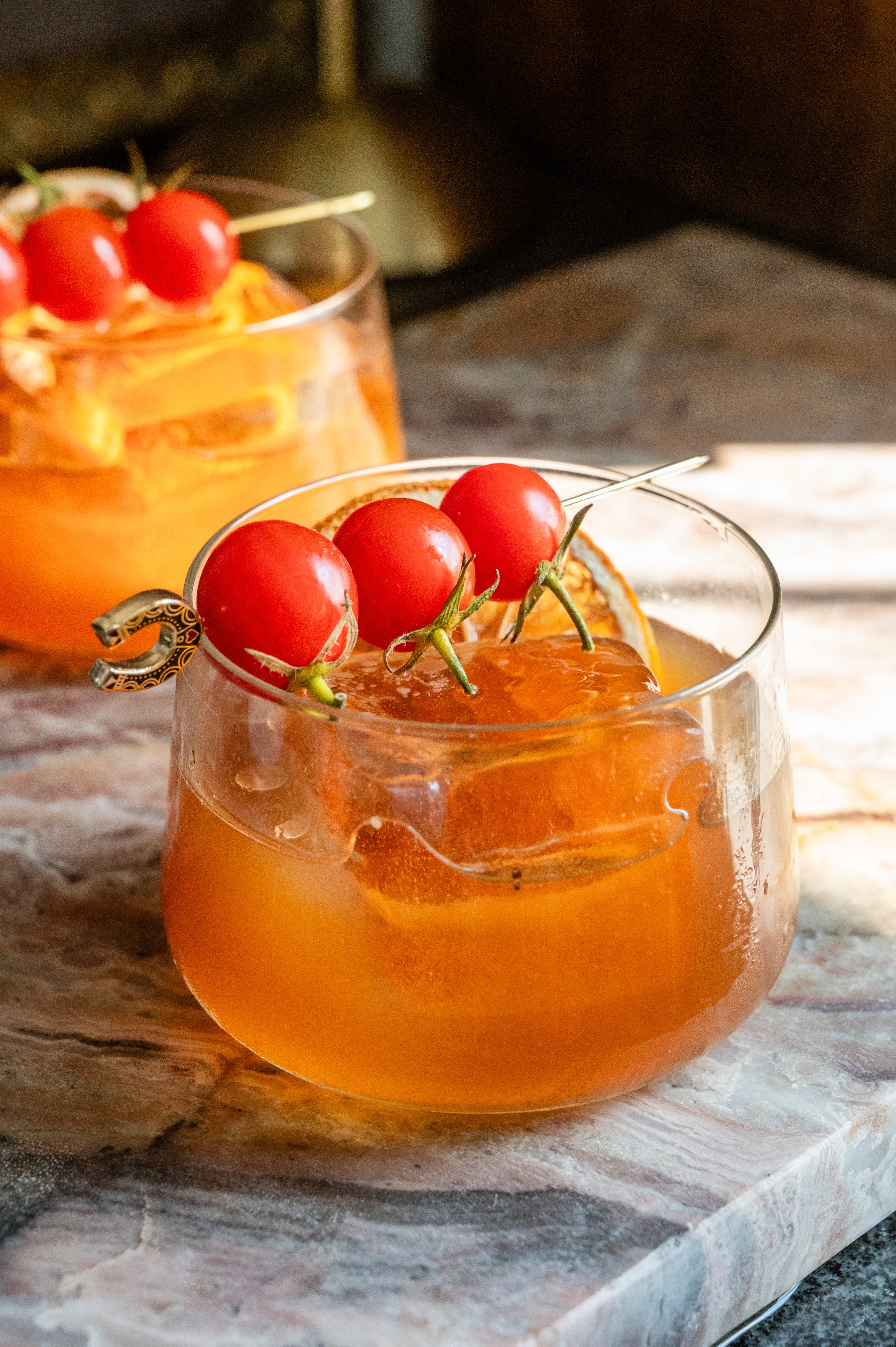 The truffle and tomato old fashioned on a pink marble slab and garnish with 3 cherry tomatoes .