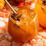 A bourbon pumpkin spritz in a pumpkin shaped glass on a orange marble table.