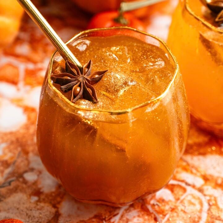 A bourbon pumpkin spritz in a pumpkin shaped glass on a orange marble table.