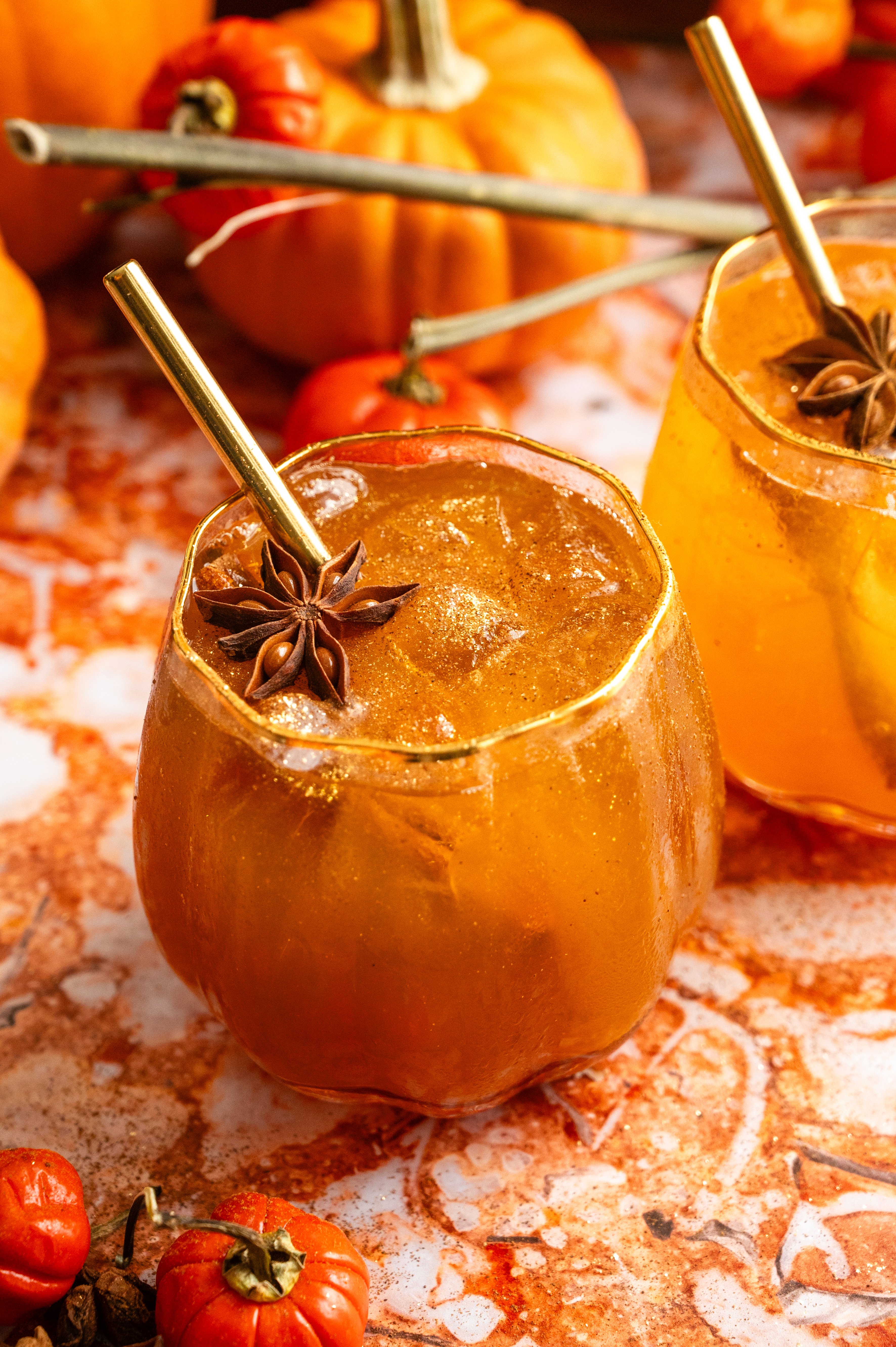 A bourbon pumpkin spritz in a pumpkin shaped glass on a orange marble table.