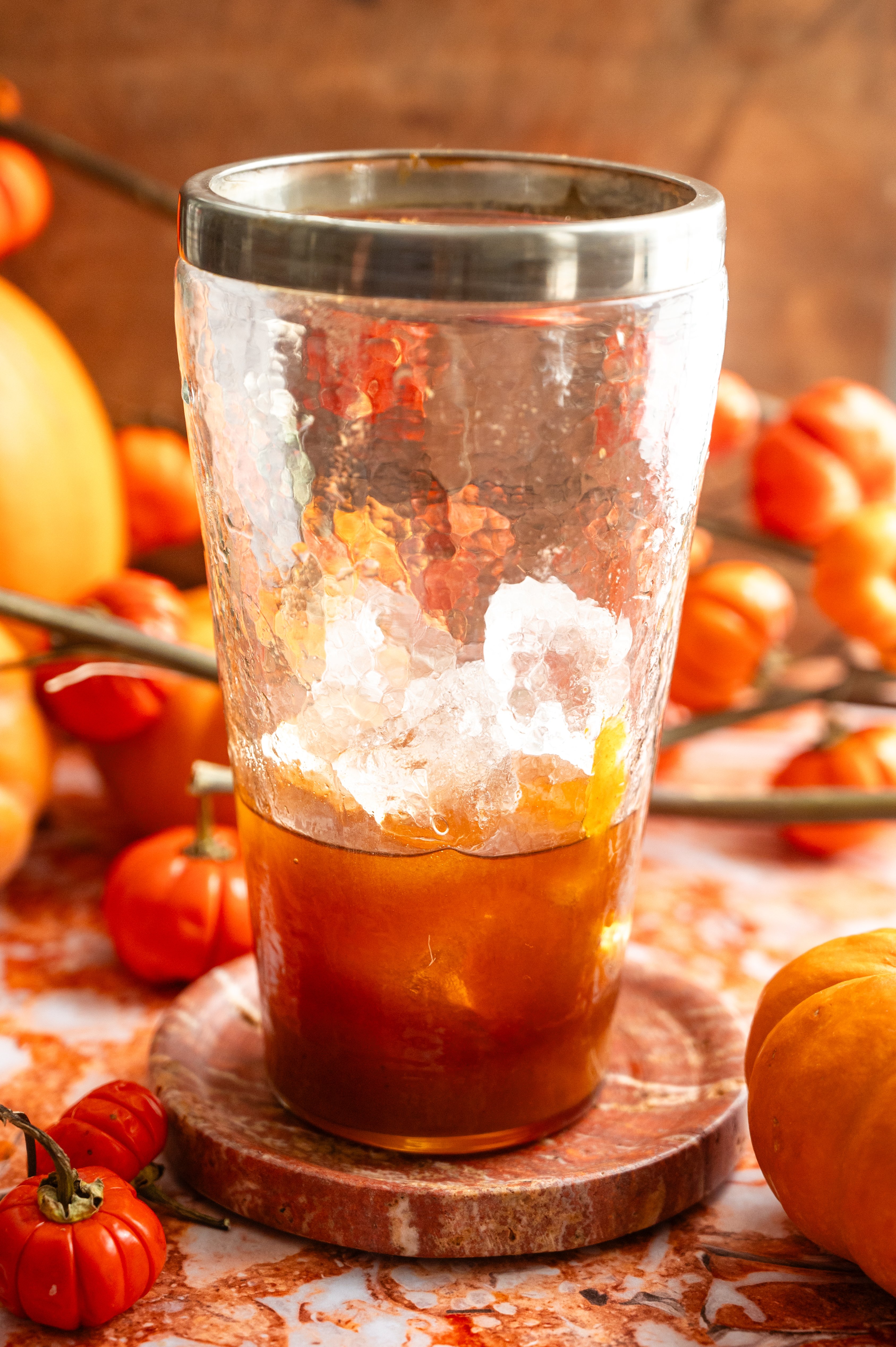 A cocktail shaker filled with ice and the ingredients on a orange marble table.