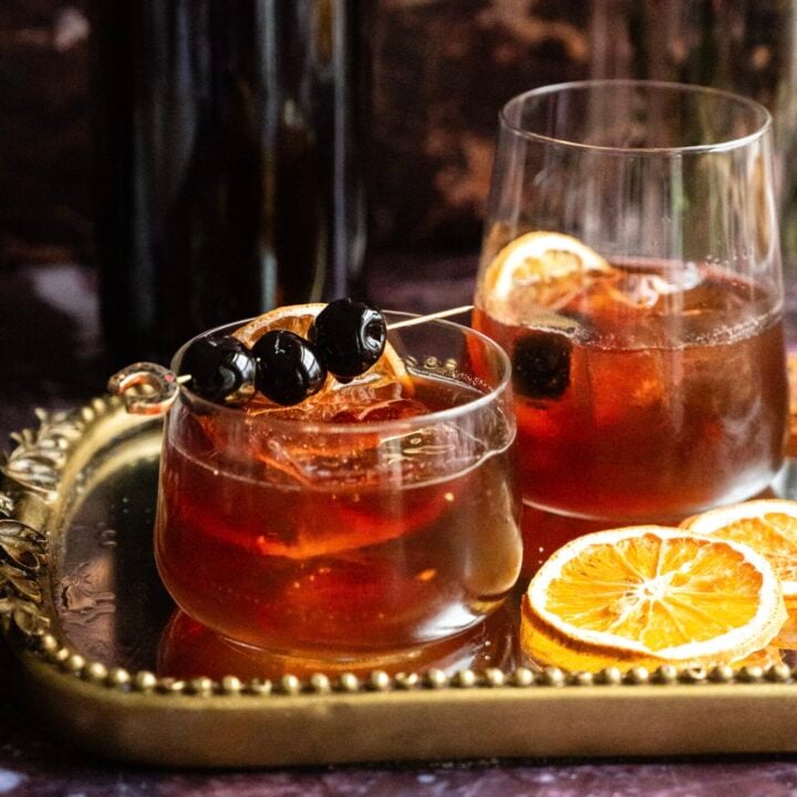 Two old fashioneds sitting on a mirrored tray with a batched container in the back ground.