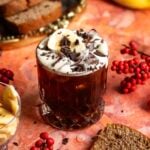 A rocks glass on an orange marble table filled with the banana bread carajillo and garnished with shaved chocolate and a banana chip.