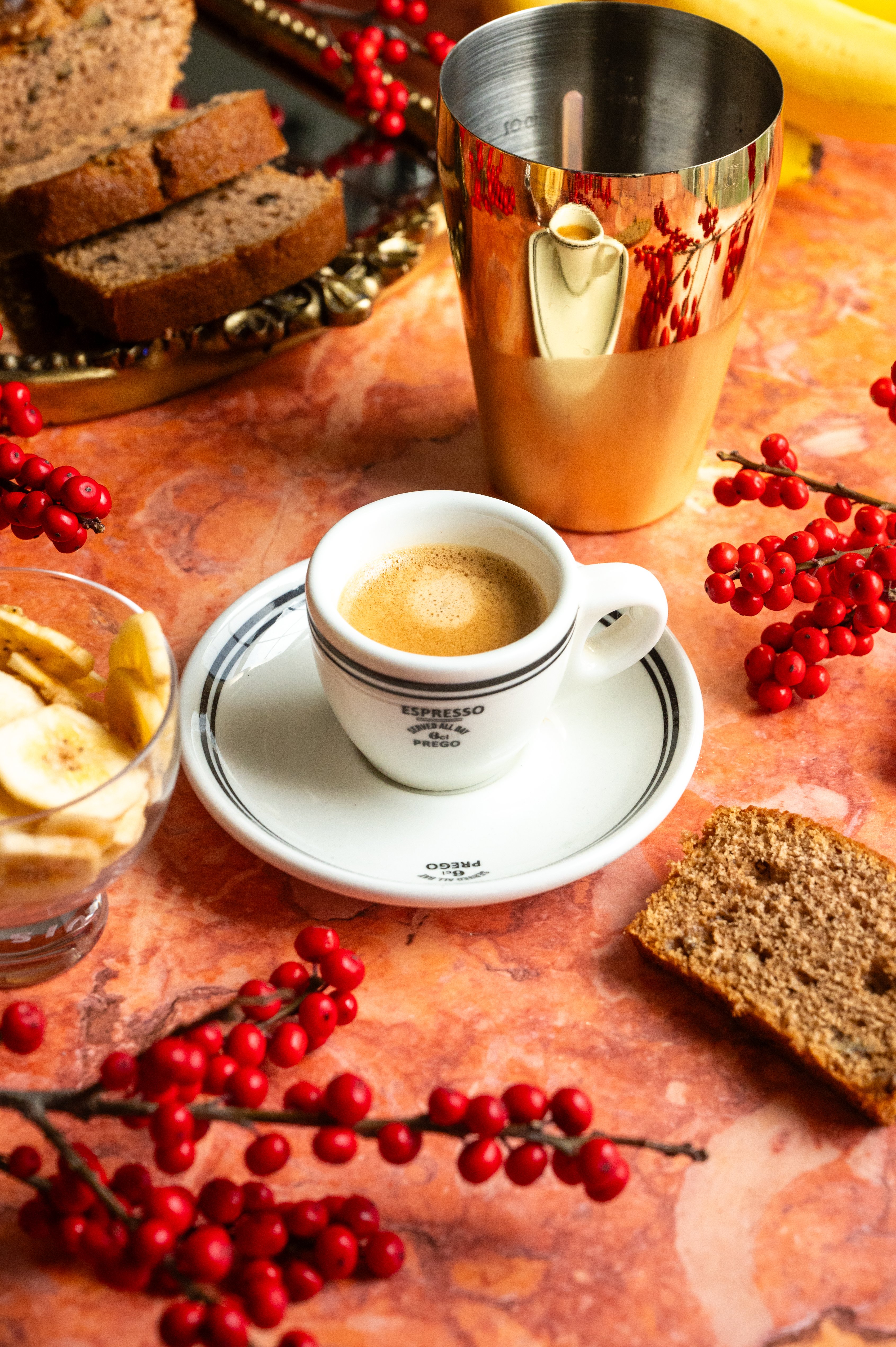 A shot of espresso on a red marble table with some banana bread by its side.