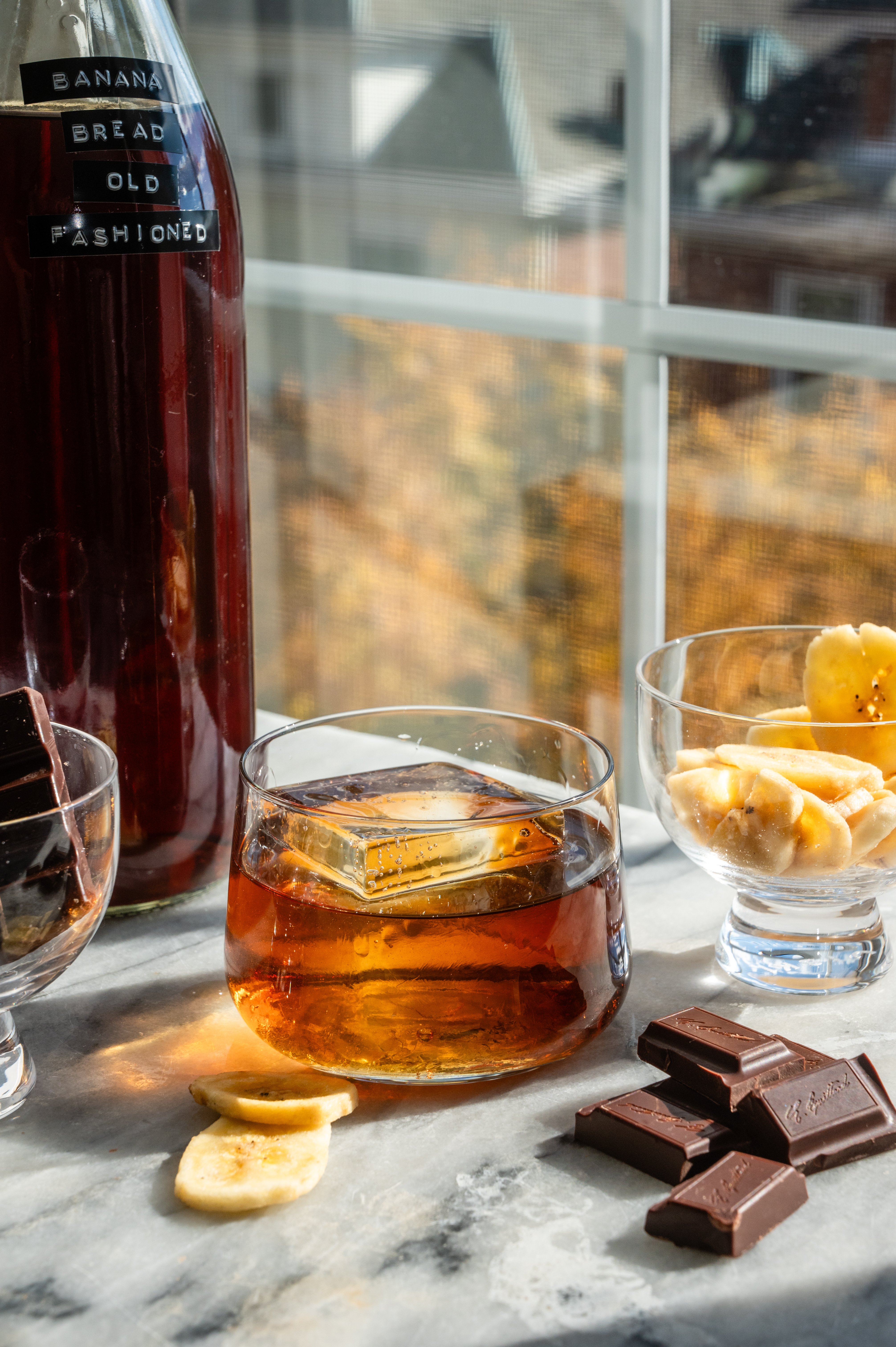 The drink has been poured over a large ice cube and Its also on a marble table in front. of a window.