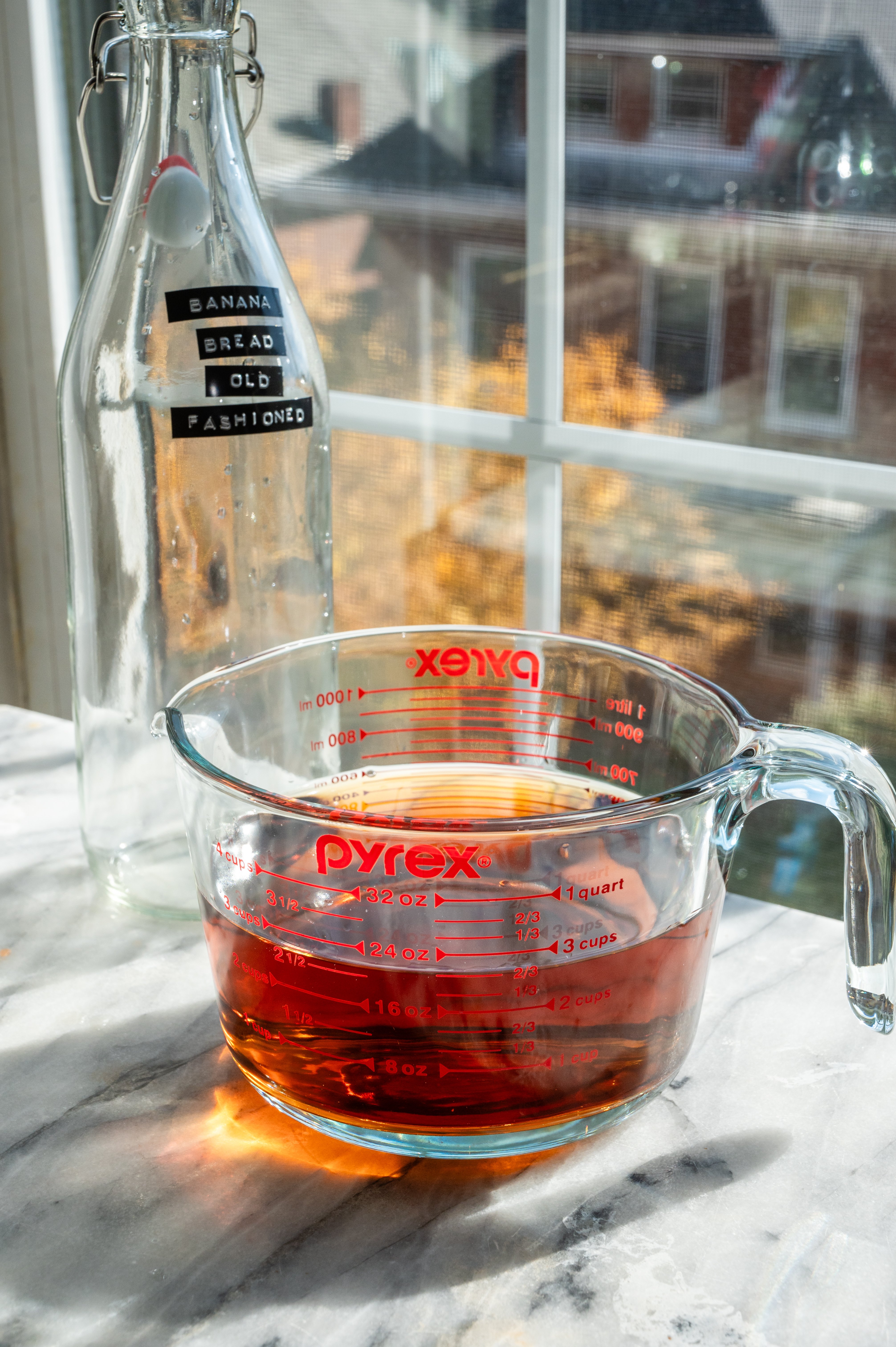 Bourbon in a large measuring cup, Its also on a marble table in front. of a window.