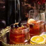 Two old fashioneds sitting on a mirrored tray with a batched container in the back ground.