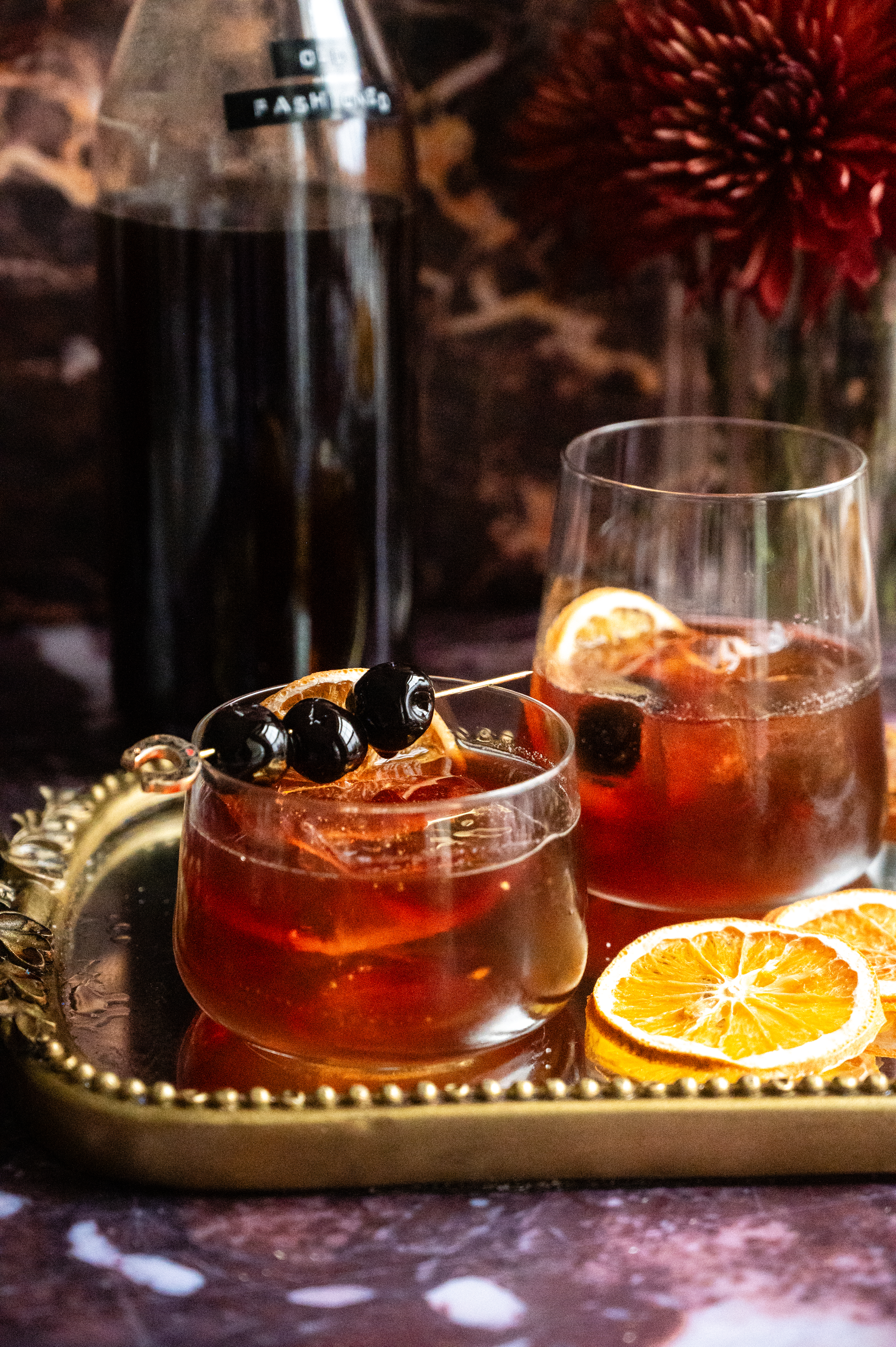 Two old fashioneds sitting on a mirrored tray with a batched container in the back ground.