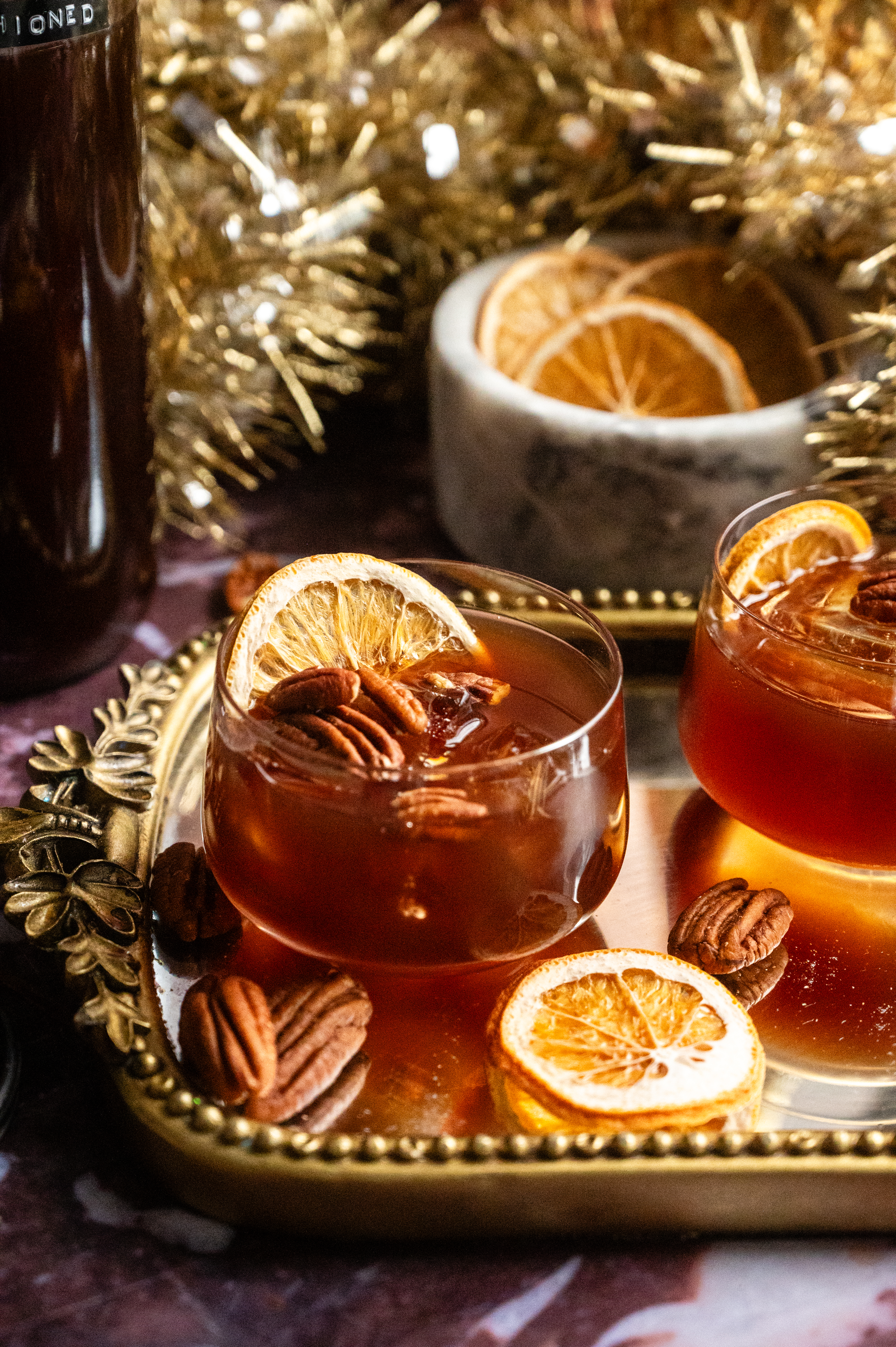 Two spiced pecan old fashioneds sitting on a mirrored tray.