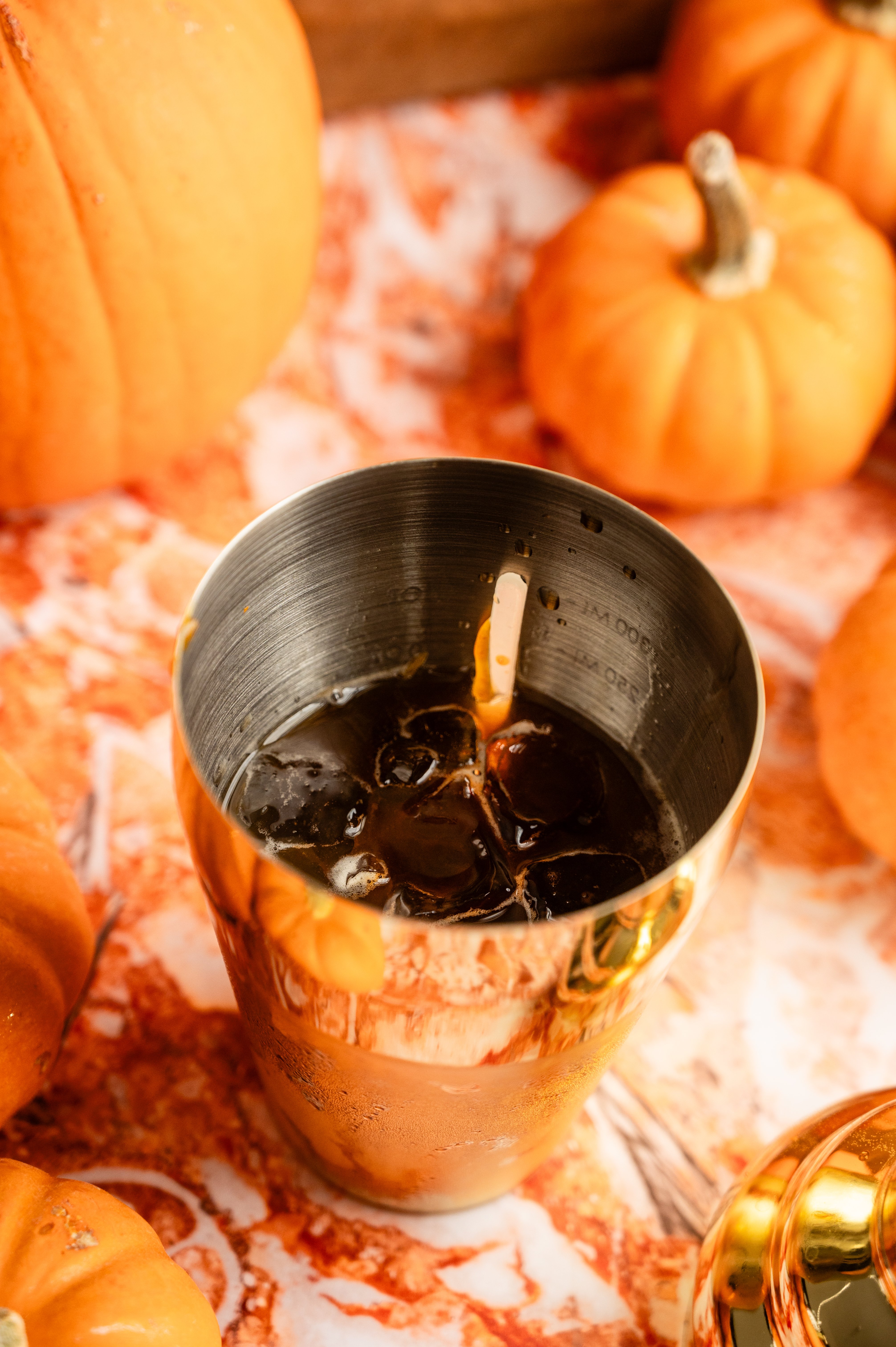 All the ingredients in a cocktail shaker on an orange marble table.