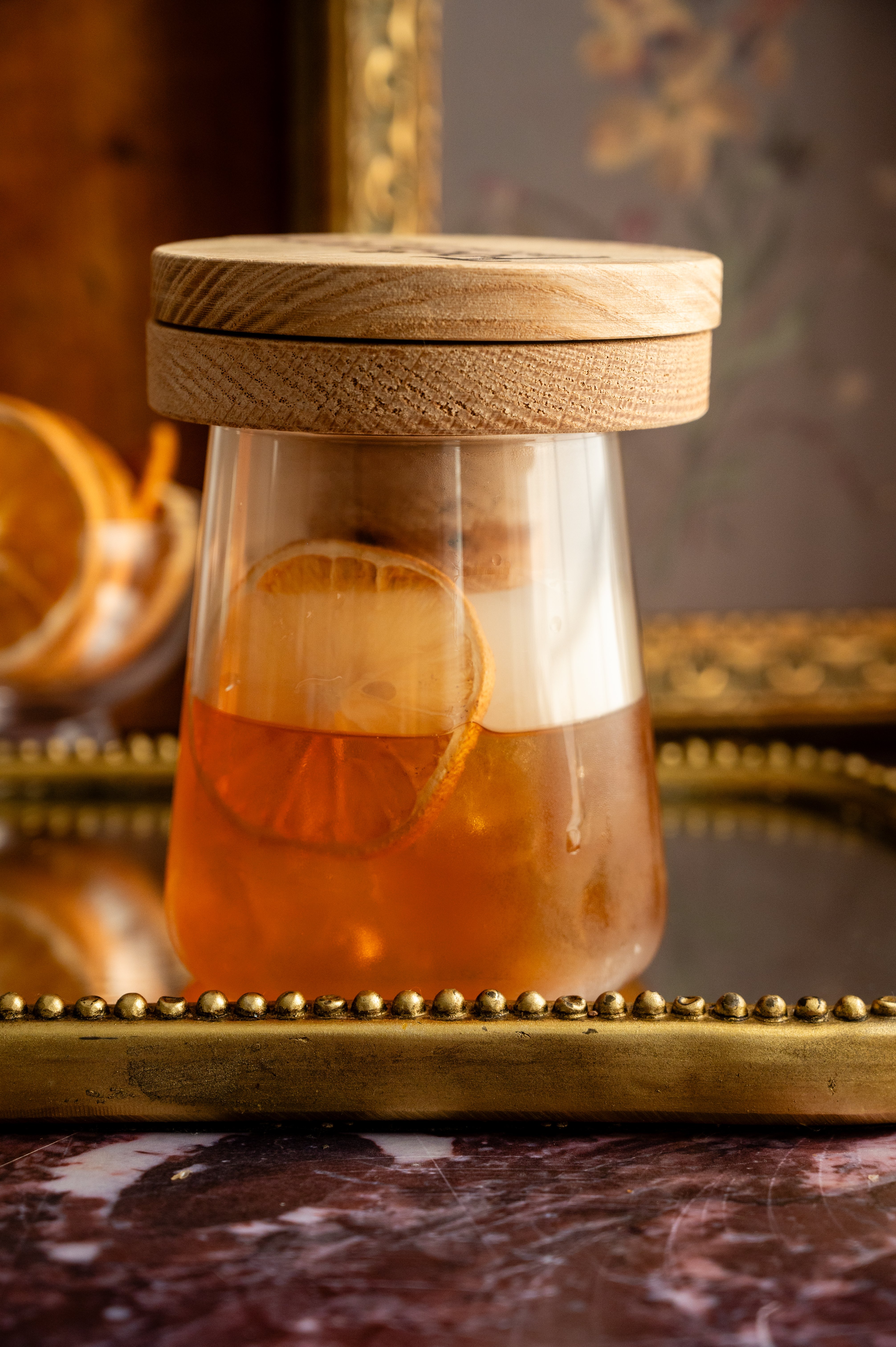 A large rocks glass filled with ice and a mixed old fashioned and topped with an individual smoker. Smoke is filling the glass.