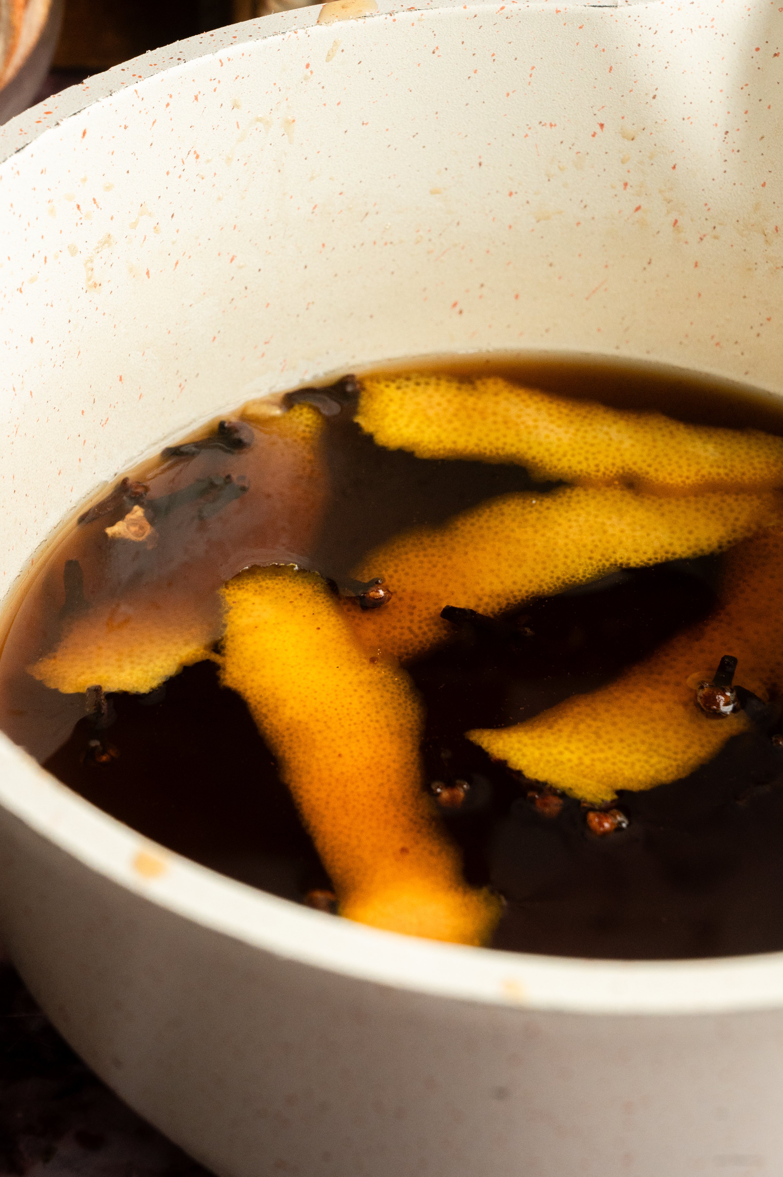 The orange and clove syrup sitting in a white pot.