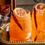 Calabrian chili margaritas on a mirrored tray and. garnished with a dried chili pepper and. dehydrated orange.