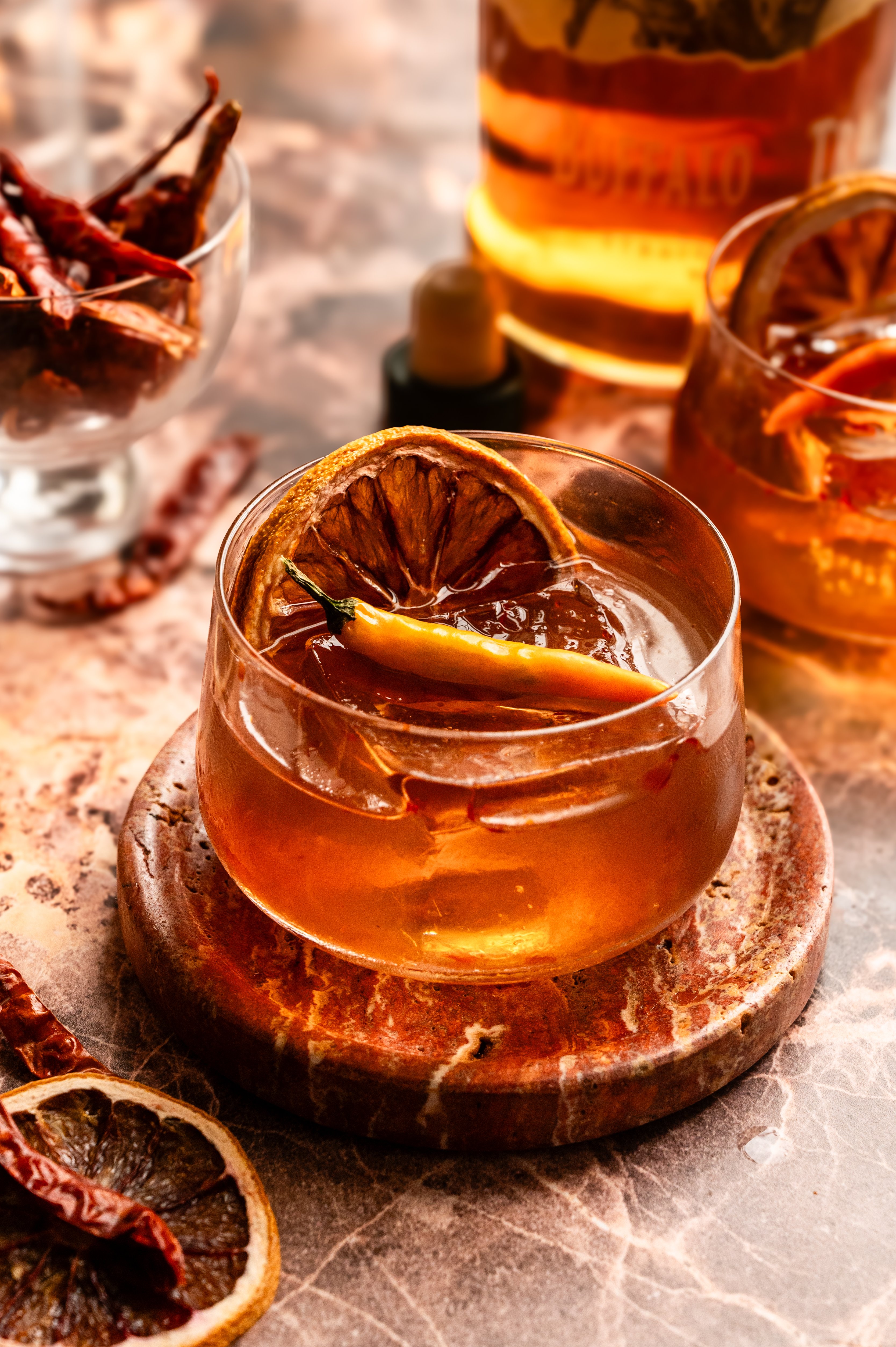 The old fashioned on a pink marble table garnished with a dehydrated orange and a this chili.