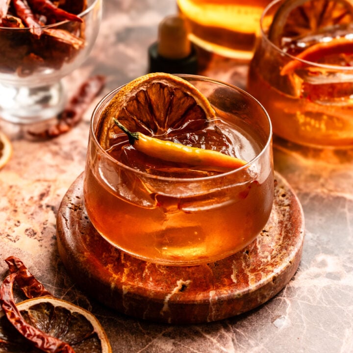 The old fashioned on a pink marble table garnished with a dehydrated orange and a this chili.