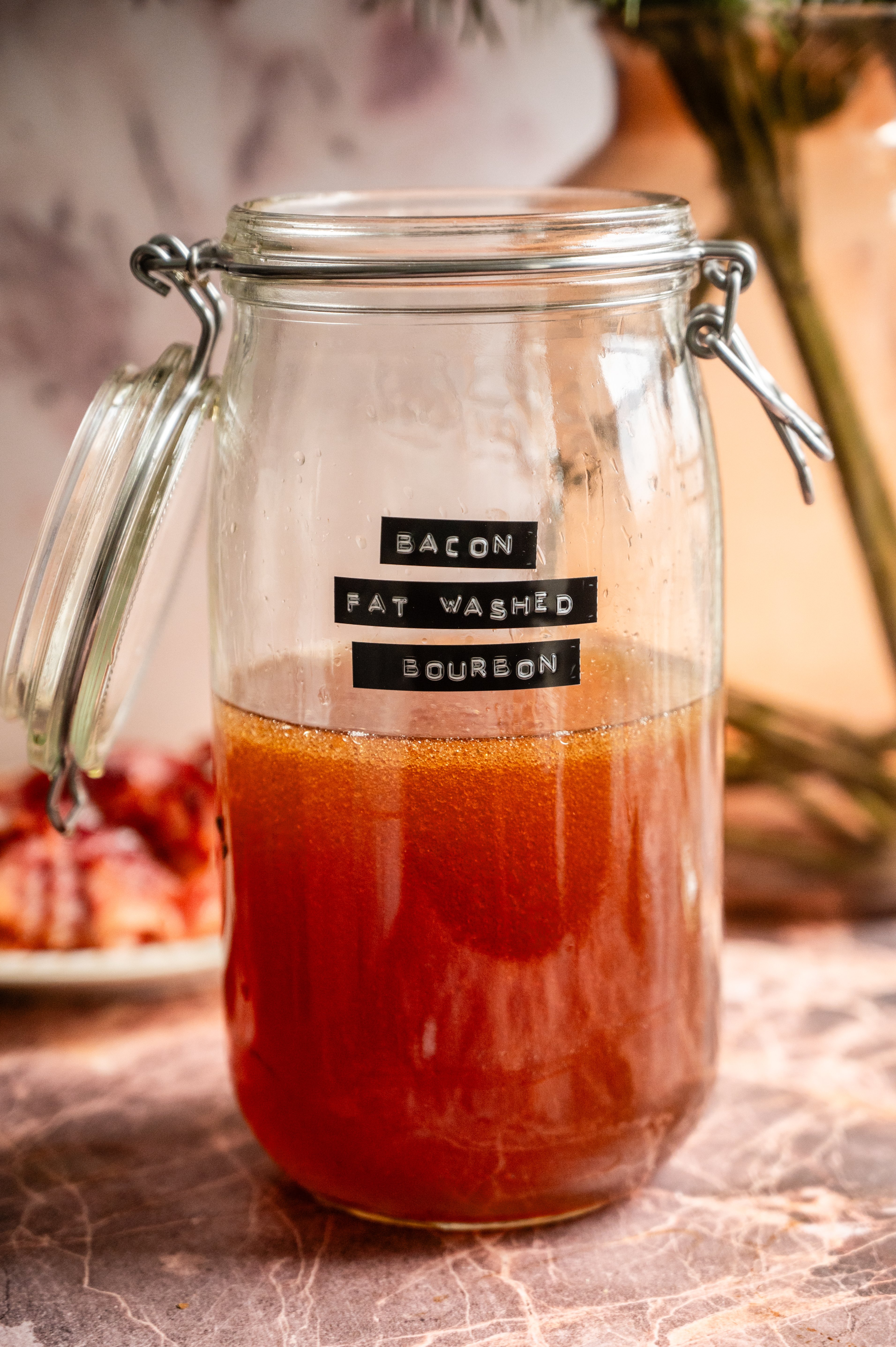 Bourbon and bacon fat in a large glass jar with the lid open.