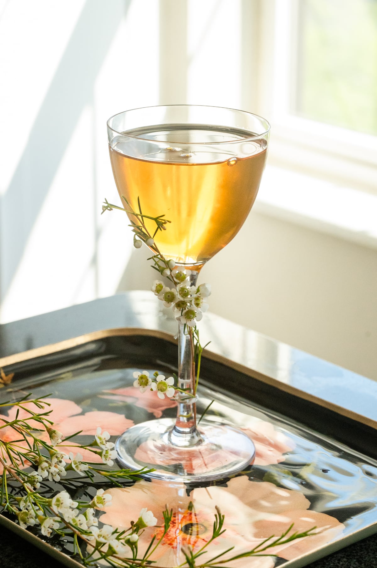 The strained cocktail in a nick and Nora glass with a white flower tied to the stem.
