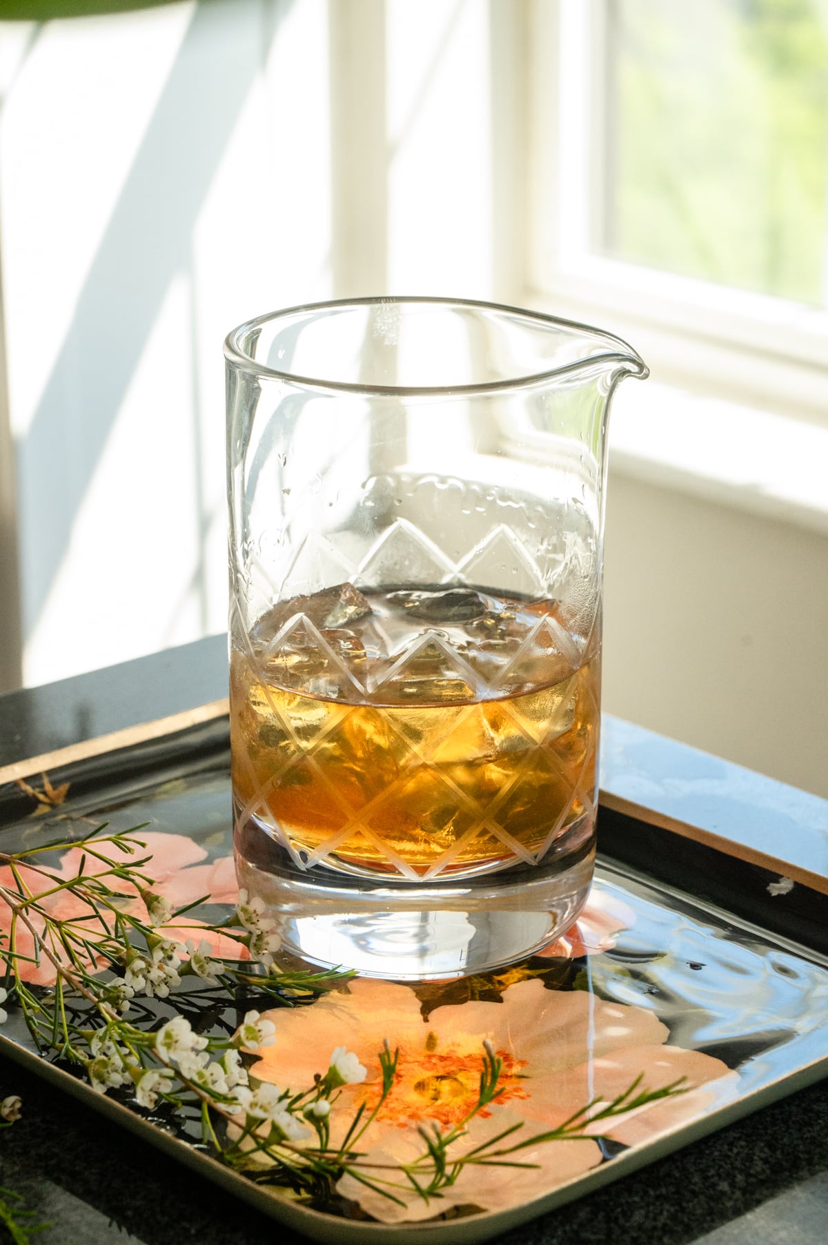 All the ingredients in a mixing. glass with ice on a pick floral tray.