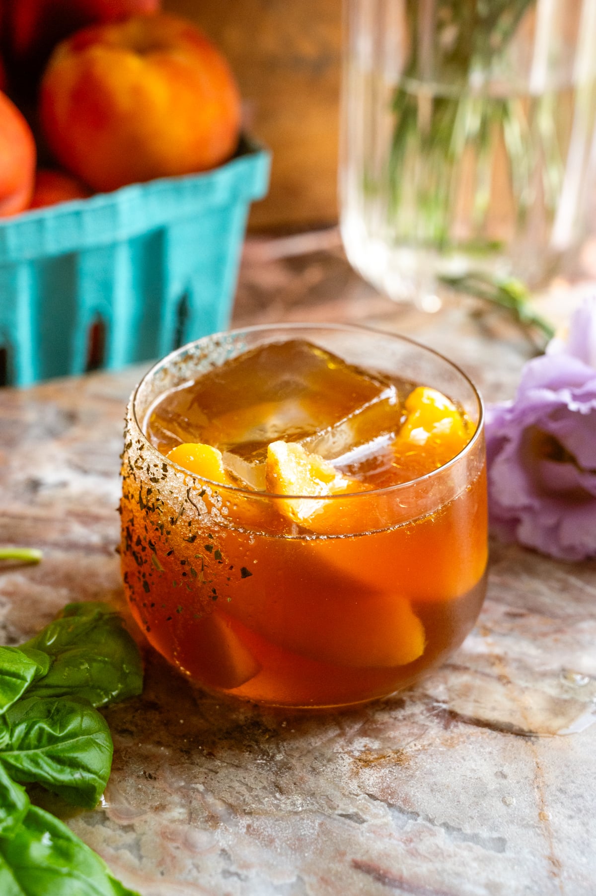 A short rocks glass filled with the cocktail and garnished with frozen peaches on a pink marble slab.