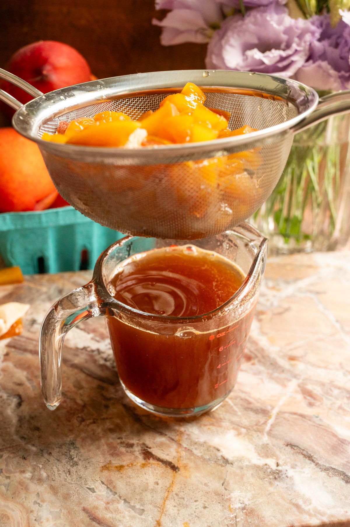 A mesh sleeve with the strained peaches sitting over a measuring cup with the syrup sitting inside.