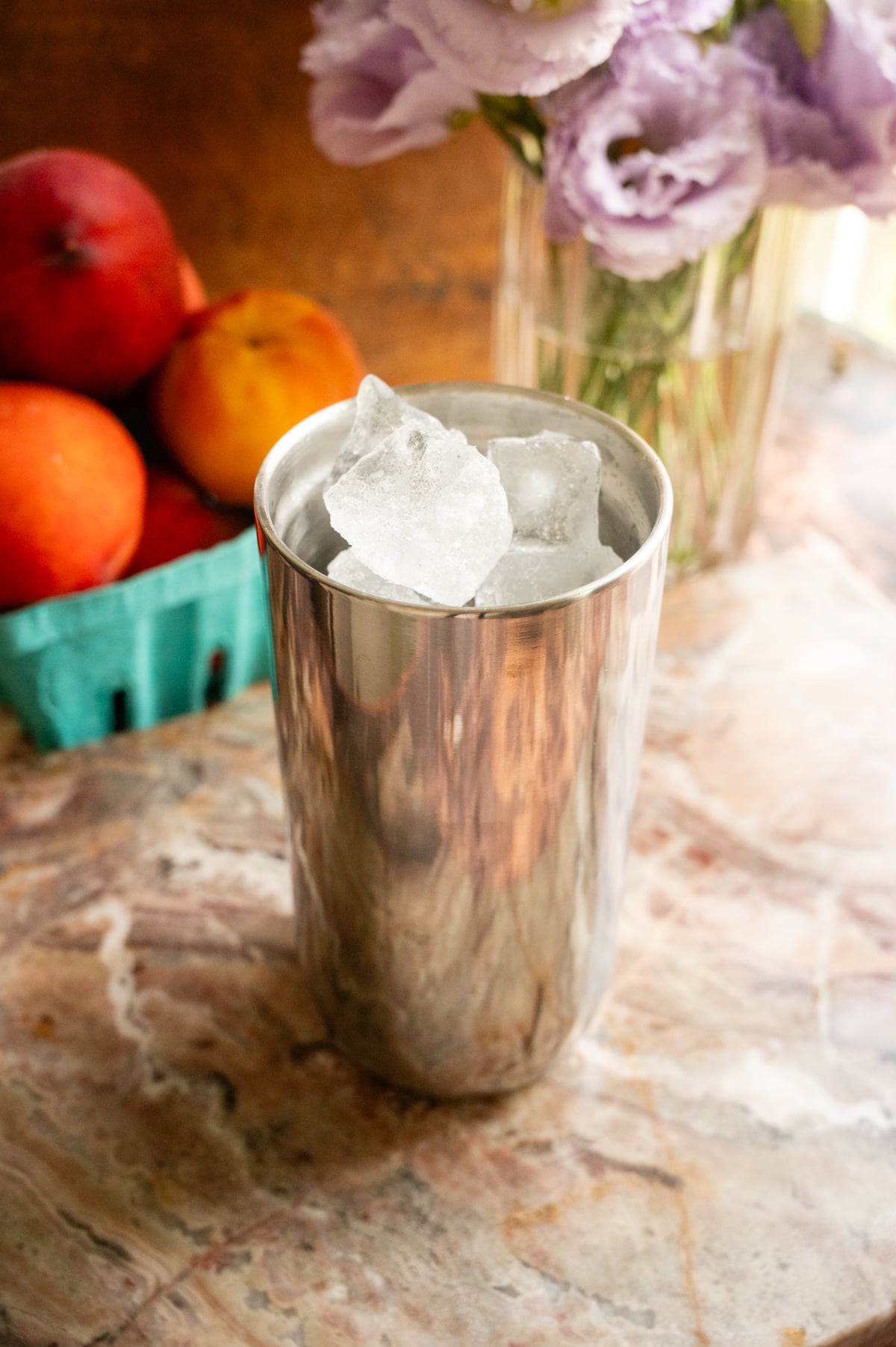 All the ingredients including the ice sitting in a sliver metal cocktail shaker.