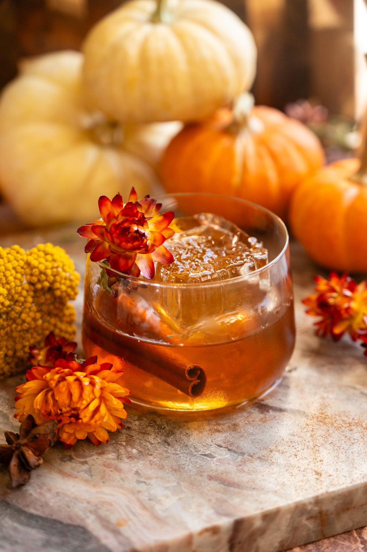 salted maple old fashioned surrounded by pumpkins and garnished with a red/yellow flower.