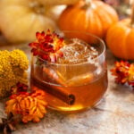 salted maple old fashioned surrounded by pumpkins and garnished with a red/yellow flower.