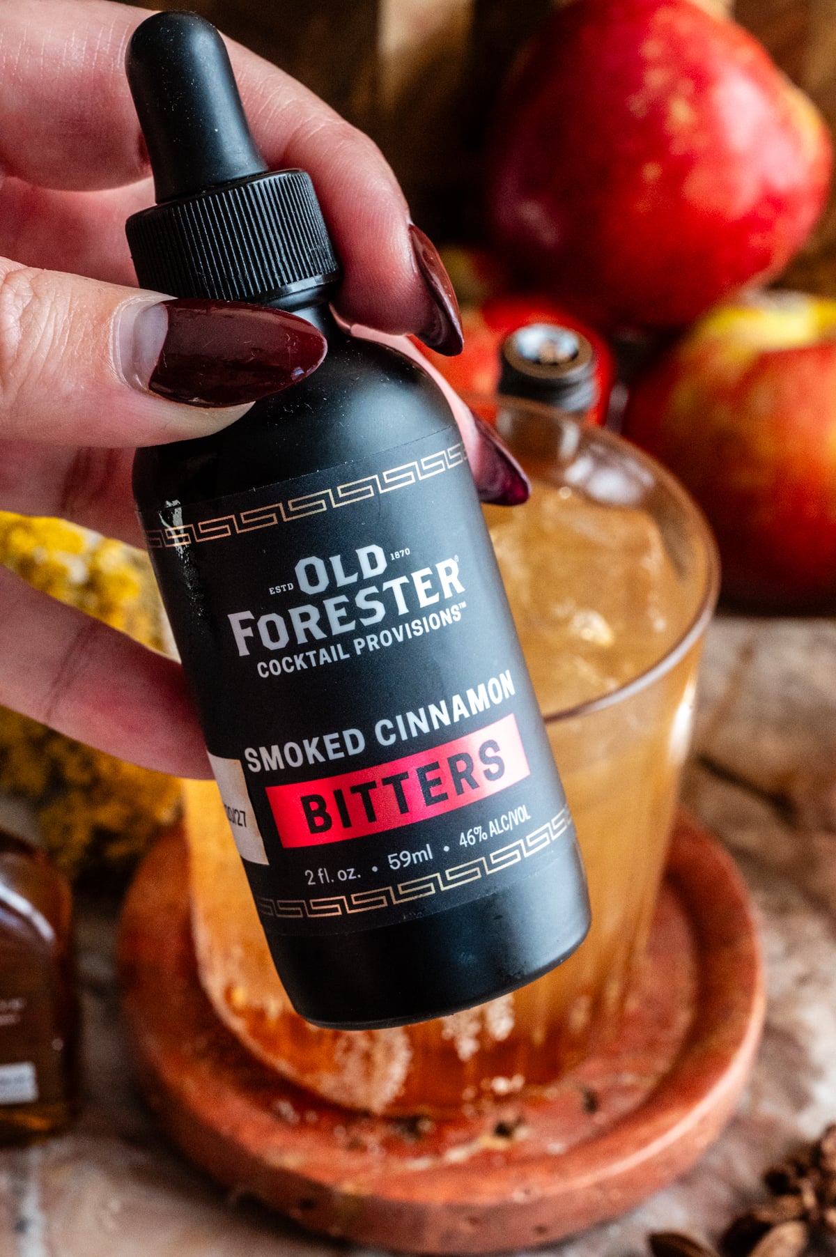 A hand holding up the cinnamon bitters for the camera.