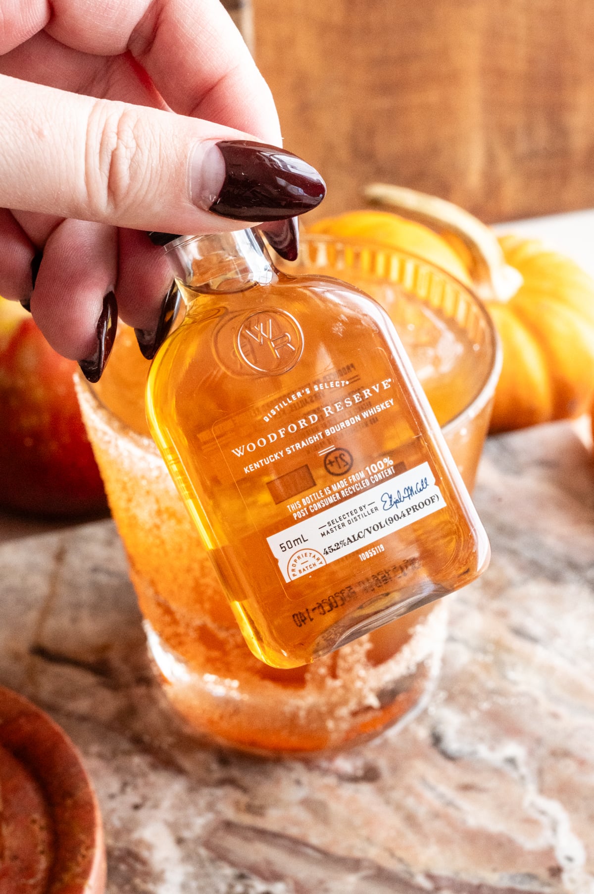 A little bottle of Woodford reserve is being held up to show the camera.