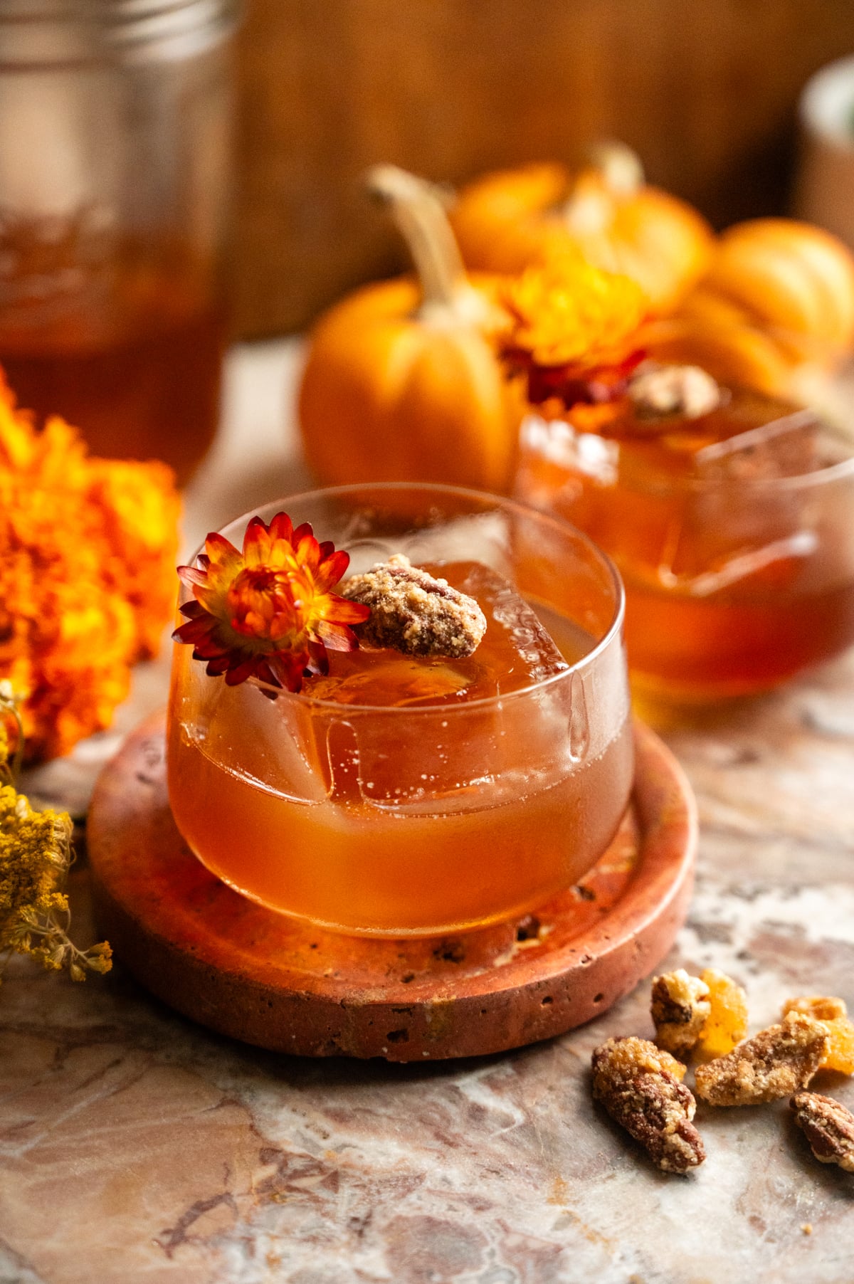 An old fashioned garnished with a pecan and dried flower on a pink marble slab.