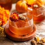 An old fashioned garnished with a pecan and dried flower on a pink marble slab.