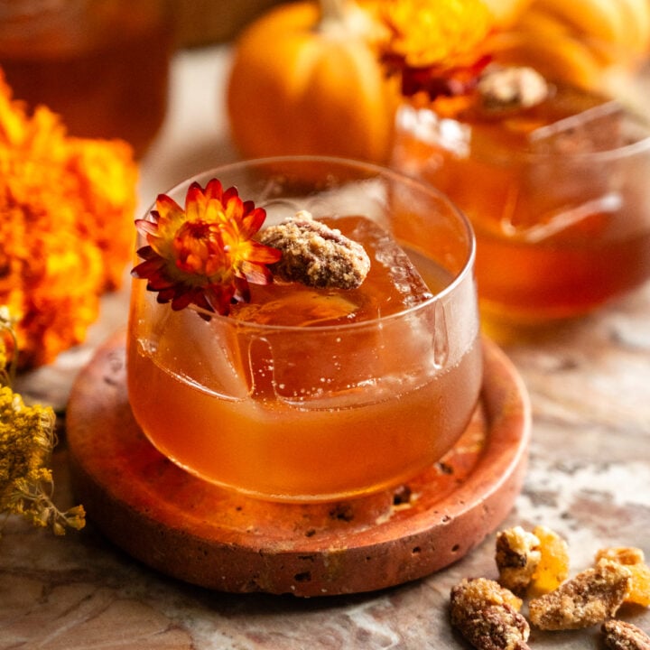 An old fashioned garnished with a pecan and dried flower on a pink marble slab.